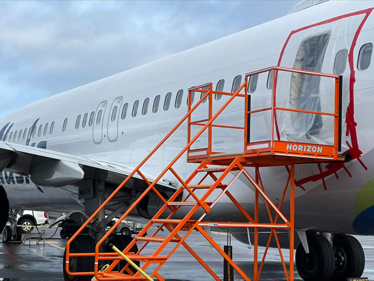 An airplane on the tarmac with a bright orange maintenance platform positioned at the open front door.