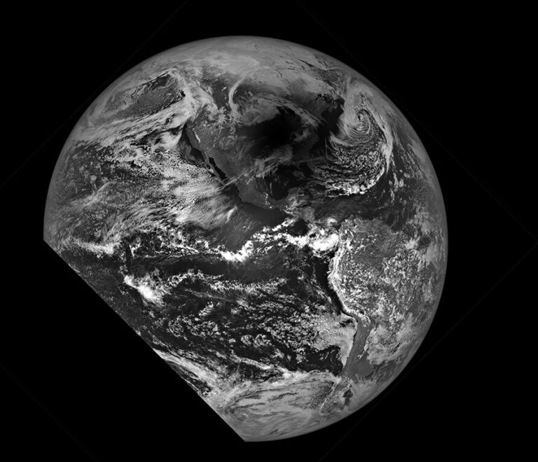 Black and white image of Earth viewed from space, showing major cloud formations and landmasses, with a shadowed area covering a portion of the Pacific Ocean.