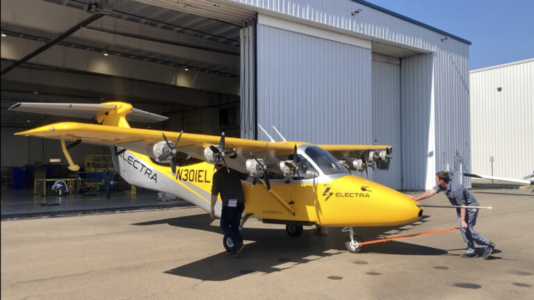 Focus increases on electric and autonomous aircraft technologies A yellow Electra aircraft is being manually pushed out of a hangar by two people on a sunny day.