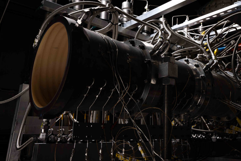Close-up of a complex machinery setup with numerous wires and metal components, possibly a part of a large industrial or scientific apparatus, in a dimly lit environment.