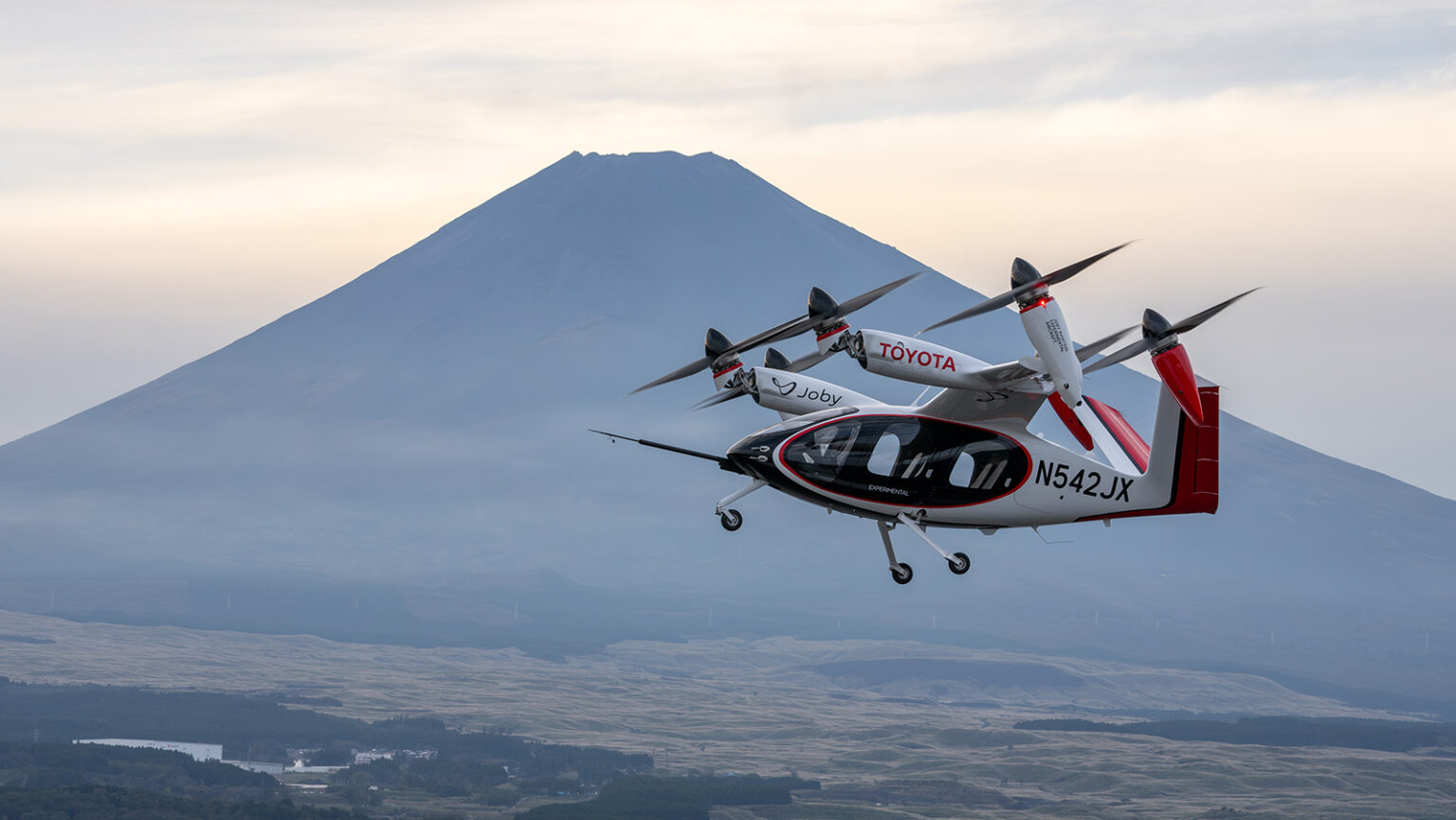 A Joby Aviation aircraft flies near Mount Fuji, Japan, against a cloudy sky.