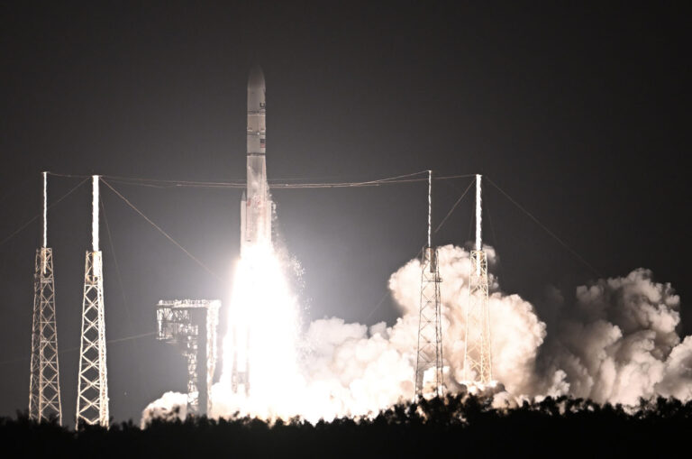 A rocket launches into the night sky, surrounded by smoke and illuminated against the darkness.