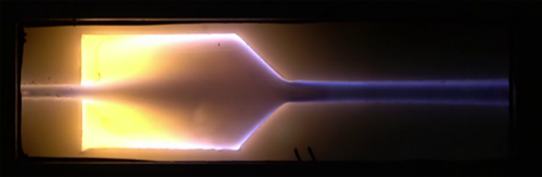A glowing plasma discharge inside a long, transparent vacuum chamber against a dark background.