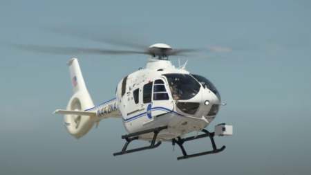 A white helicopter with blue stripes flies against a clear blue sky.