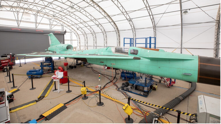 A year of new dynamic tests and facilities A large aircraft under construction or maintenance inside a hangar, surrounded by equipment and safety barriers.
